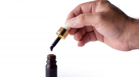 Hand holding pipette of Cannabis oil over a bottle